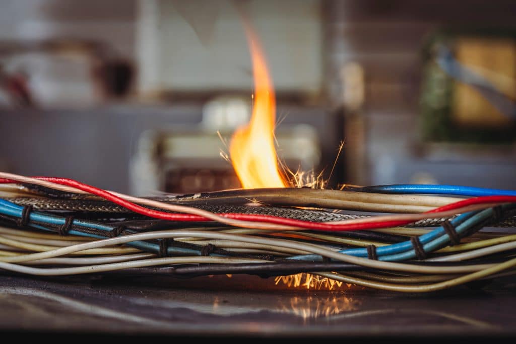 Flames, sparks, smoke between electrical cables, closeup. Short circuit in the twisted wires from the electrical devices, fire hazard concept