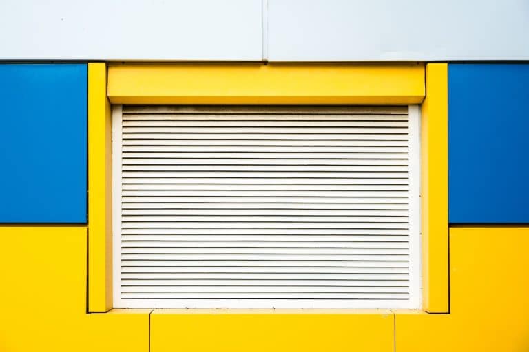 Closeup shot of a yellow and blue wall with closed window shutter