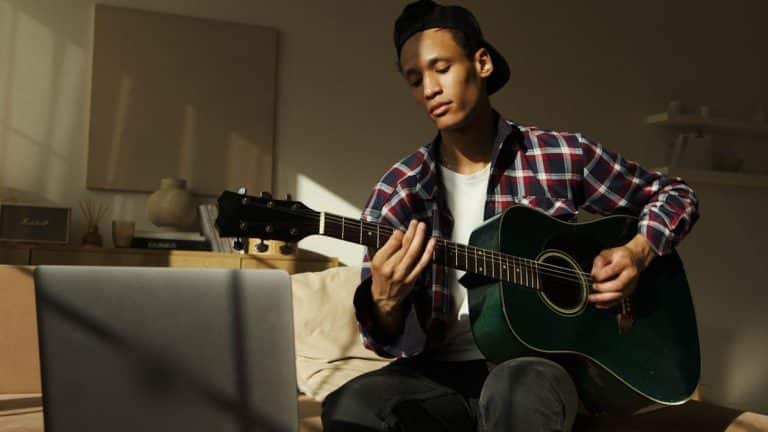 Free Young man playing guitar indoors during the day, wearing casual clothes. Stock Photo