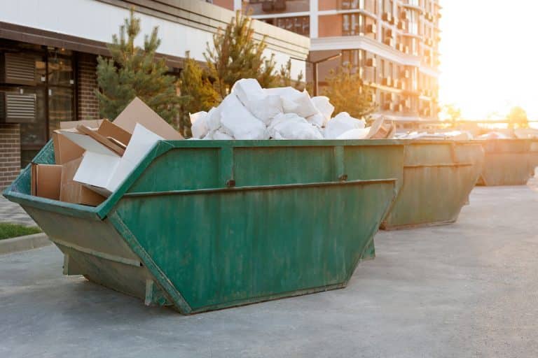 Garbage cans stand next to a house under construction at sunset. Container with construction debris.
