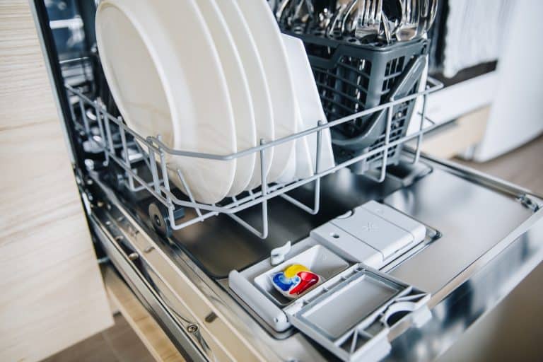 Colorful dishwasher detergent tablet for dishwashing machine. Open dishwasher with clean glasses and dishes close-up in modern kitchen.