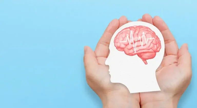 Hands holding paper cutout of a head with brain illustration on blue background