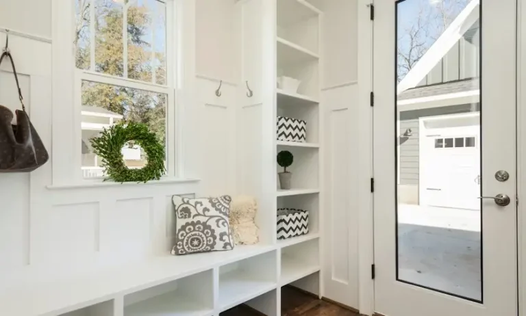 Bright mudroom entryway with white shelving, decorative pillows, and a greenery wreath by the window