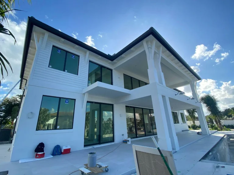 Modern white two-story house under construction with glass windows and large patio area