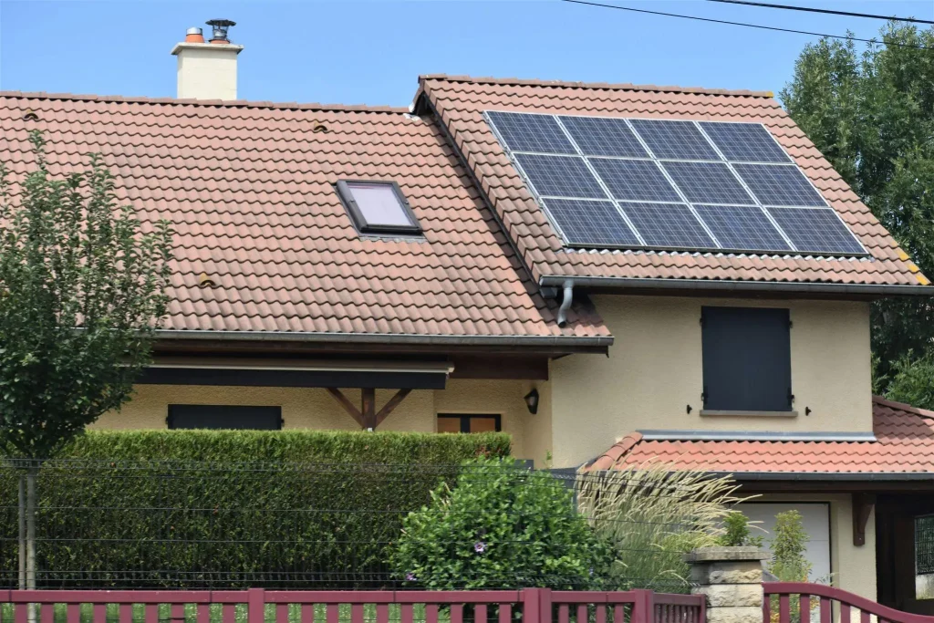 House with solar panels on red tile roof and green hedge in suburban area