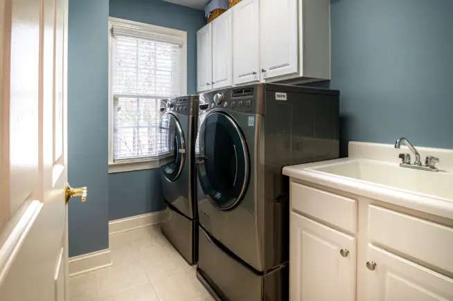 Laundry room with side-by-side front-load washers, blue walls, and white cabinetry