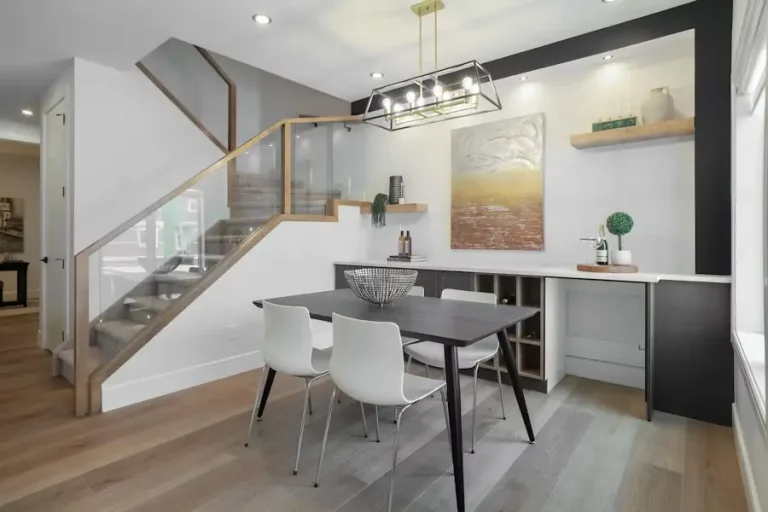 Modern dining area with wooden table, white chairs, and contemporary lighting under stairs
