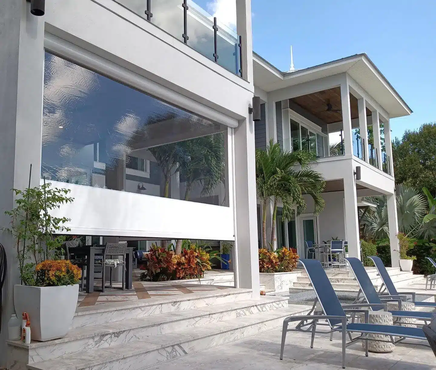 Modern beachfront house with marble steps, outdoor seating, and tropical plants in bright sunlight