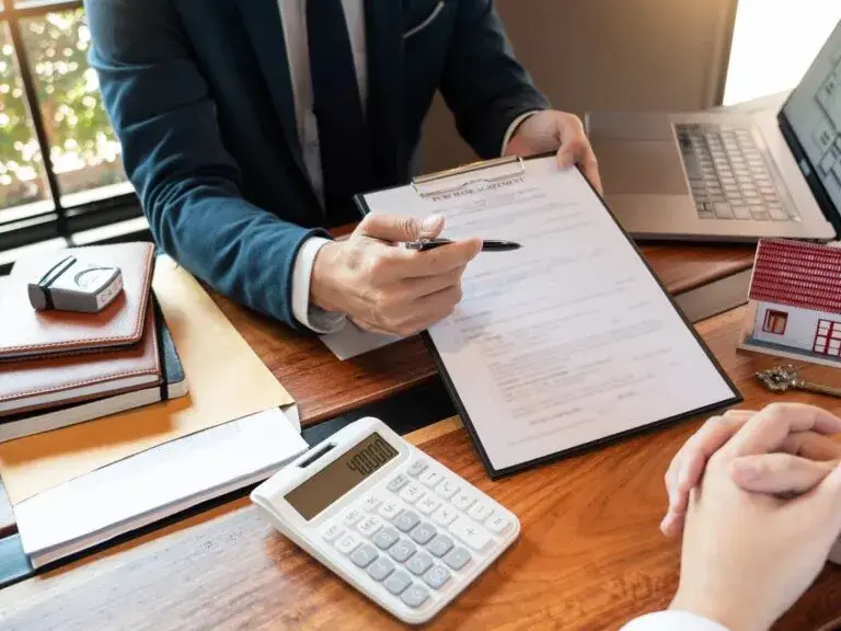 Business person in suit reviewing contract at wooden desk with calculator and laptop
