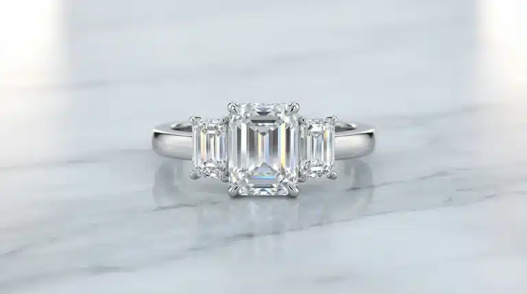 Three-stone diamond ring with emerald-cut diamonds on silver band displayed on marble surface