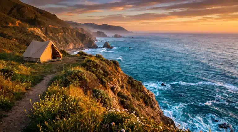 Tent on grassy cliff overlooking ocean at sunset with rugged coastline and wildflowers