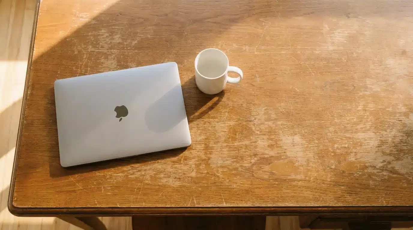 Laptop and coffee mug on wooden table under natural sunlight