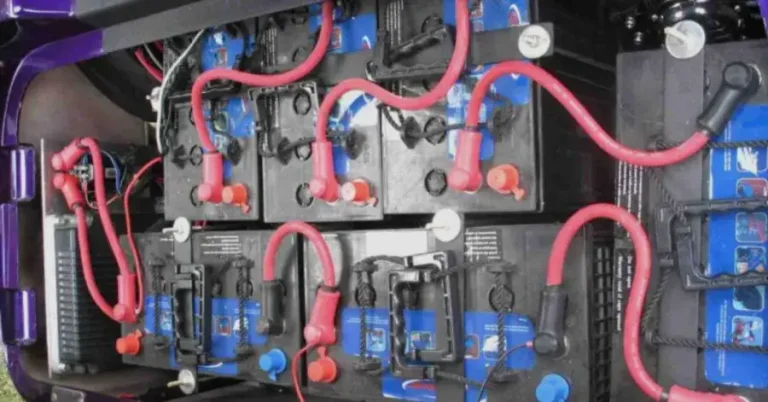 Array of interconnected batteries with red and black cables in a mechanical compartment