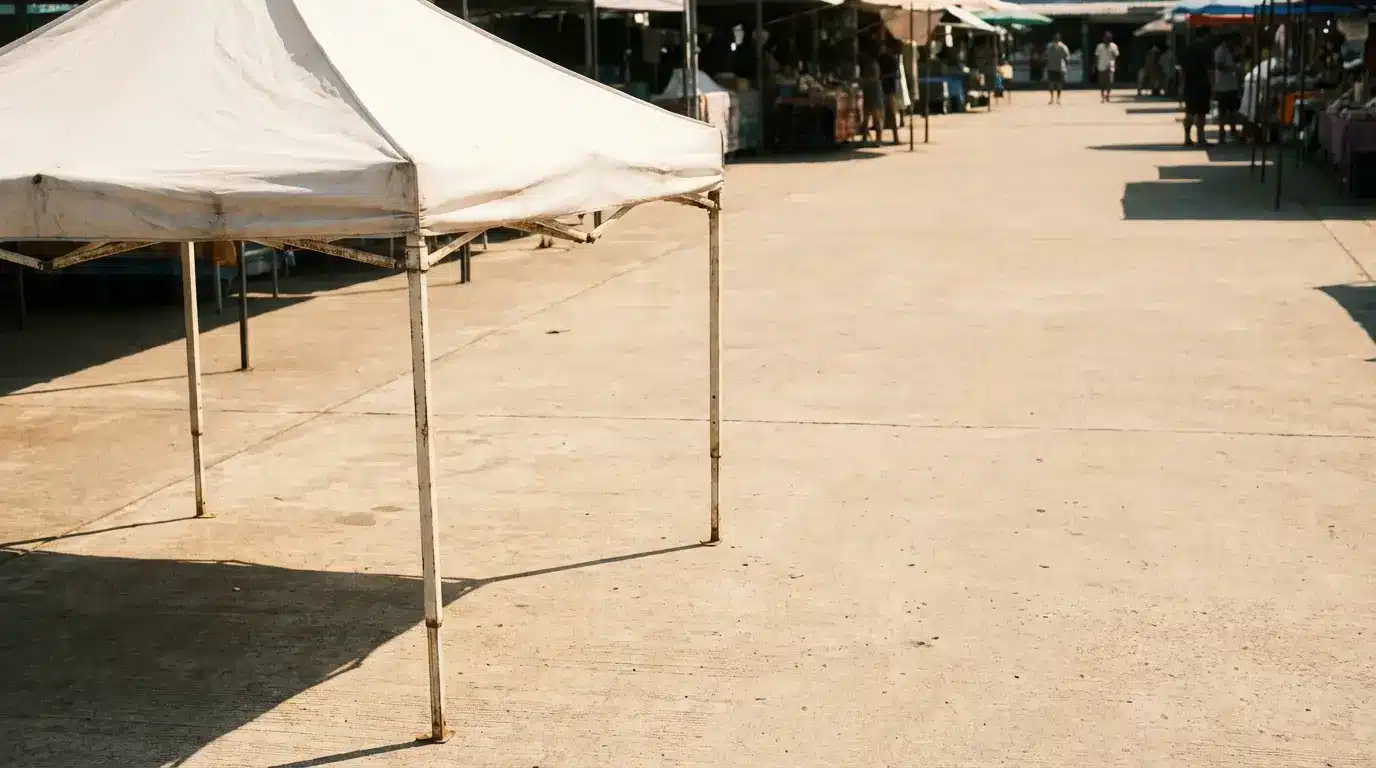 Empty white canopy tent in outdoor market with stalls in the background under sunlight