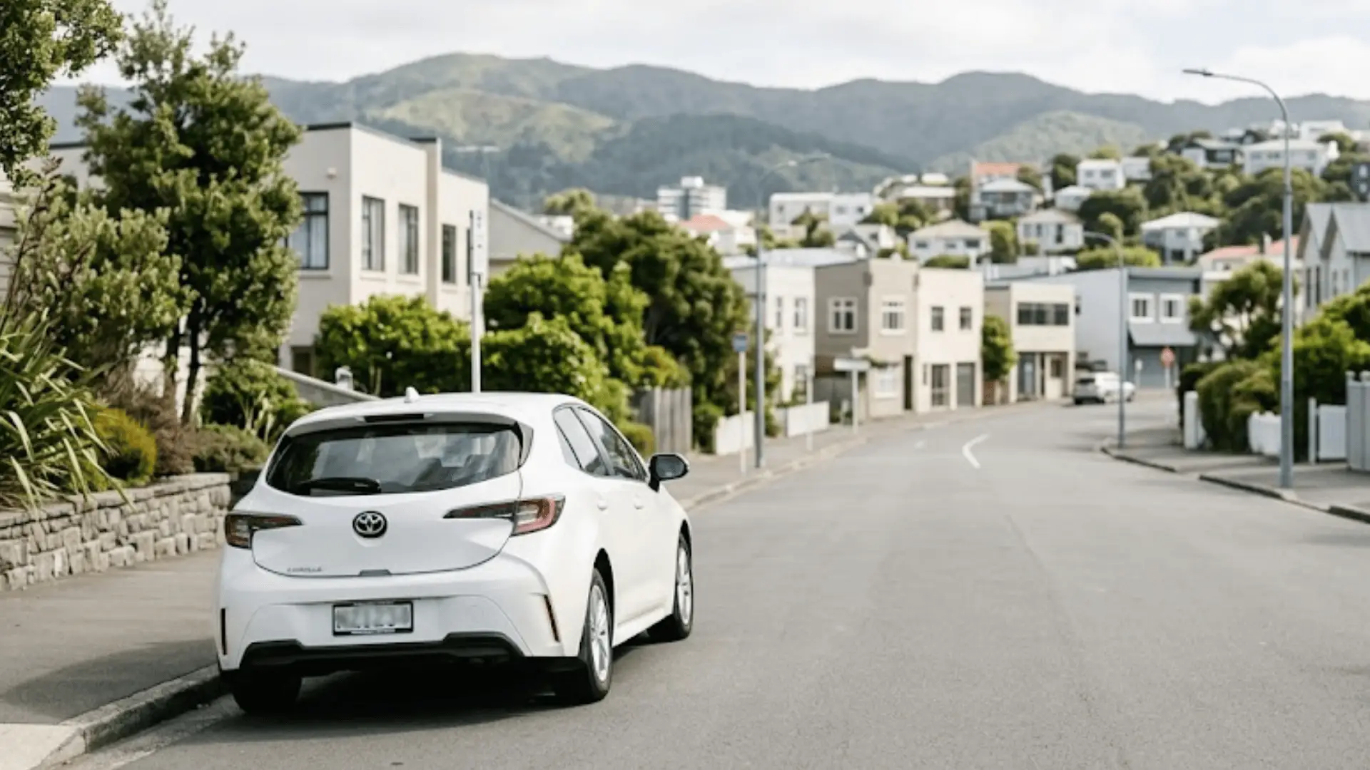 White car parked on quiet residential street with green hills in background