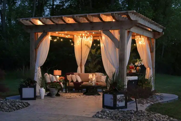 Wooden pergola with string lights and draped curtains in an illuminated garden setting