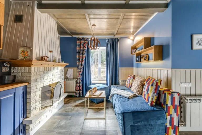 Cozy living room with blue sofa, colorful cushions, and brick fireplace under wooden ceiling