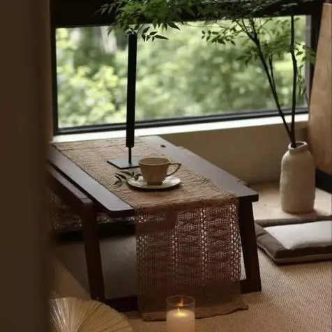 Cozy room with low wooden table, teacup, and candlelight near large window with greenery
