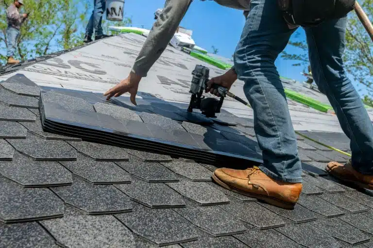 Worker installing asphalt shingles on roof with nail gun in bright outdoor setting