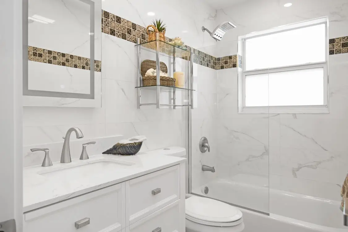 Modern white bathroom with marble tiles, glass shelf, and silver fixtures under natural light