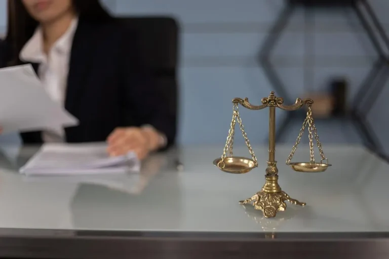 Bronze balance scale on glass desk with person reading documents in office setting