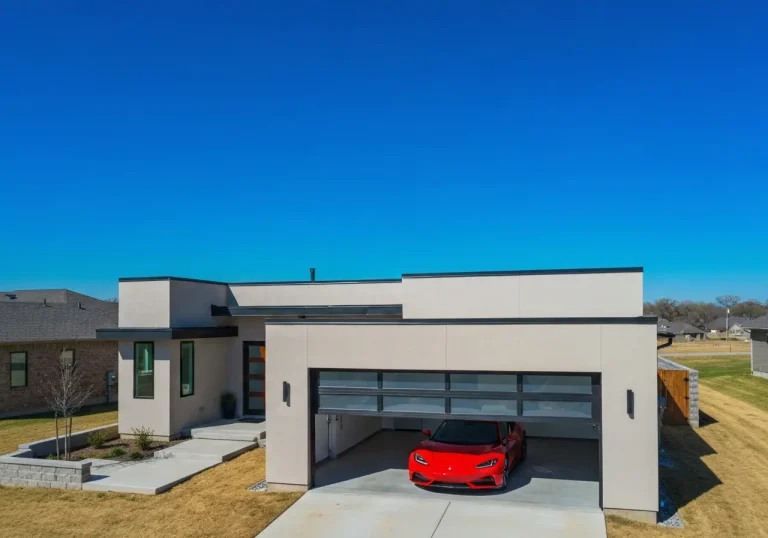 Modern single-story home with a red sports car in partially open garage under clear blue sky