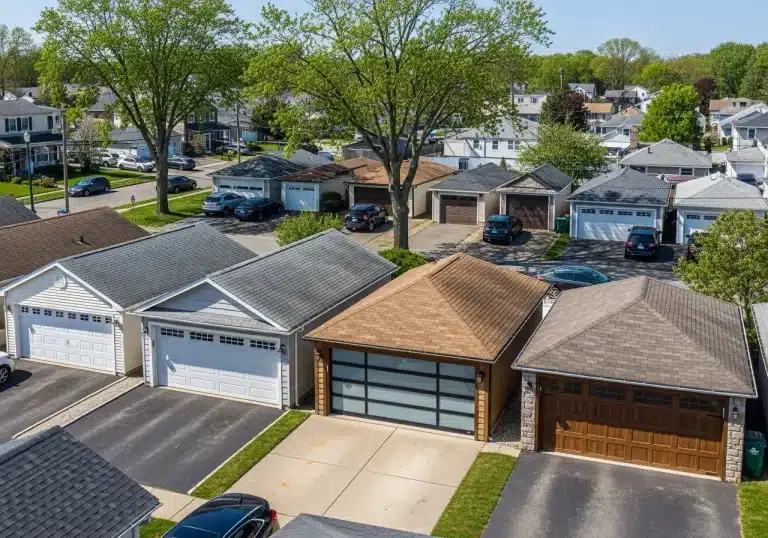 Row of suburban garages with varied roofing, cars parked in driveways, lush trees in background