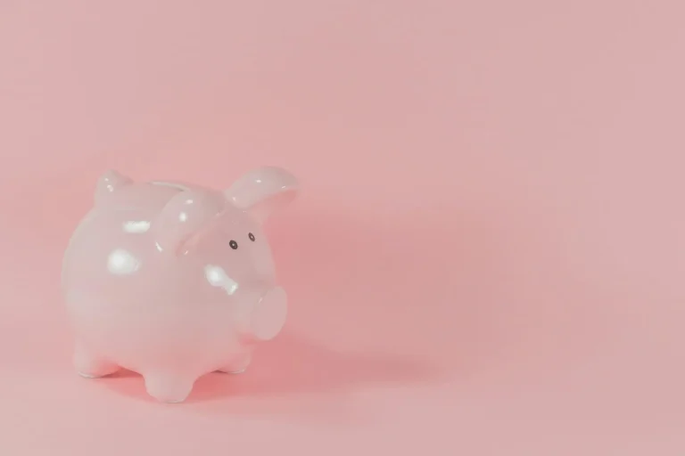 Pink ceramic piggy bank on light pink background in soft lighting