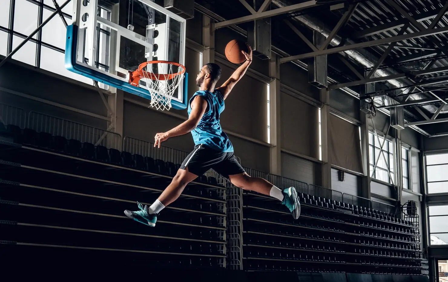 Basketball player performing a slam dunk in an indoor gym with high ceilings