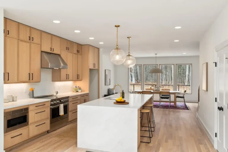 Modern kitchen with wooden cabinets, marble island, pendant lights, and dining area with large windows
