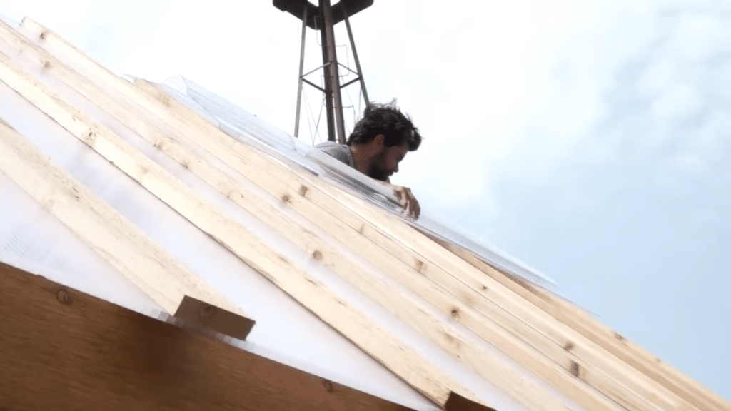A person is installing roofing material on a pitched roof while standing on top of it.