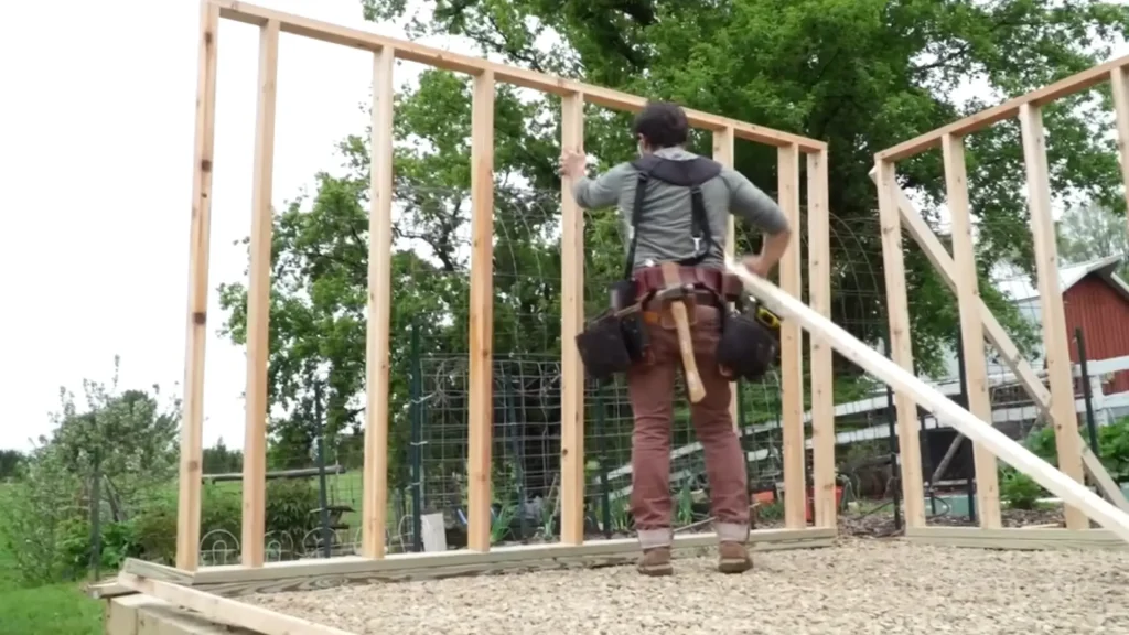 A person positions a wooden support beam against a newly framed wall in a construction site.