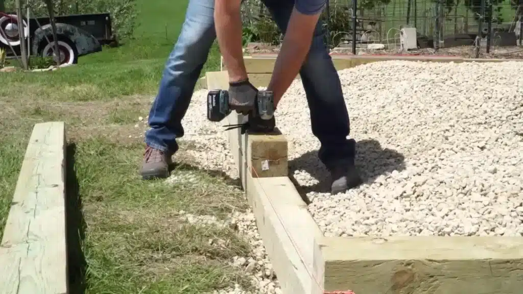 A person uses a drill to secure a wooden beam to the foundation during construction.