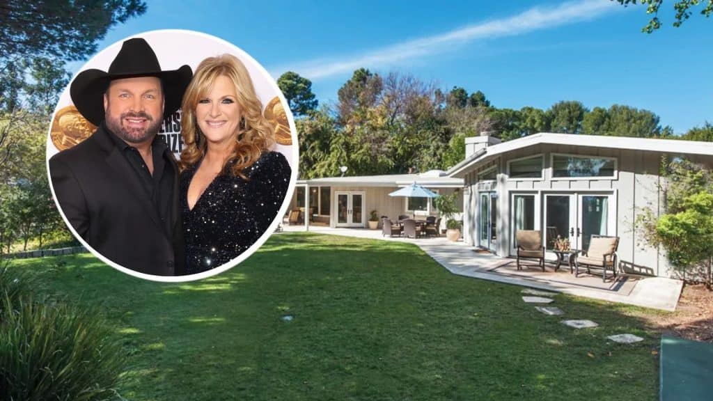 Garth Brooks and Trisha Yearwood posing together with their real estate property in the background