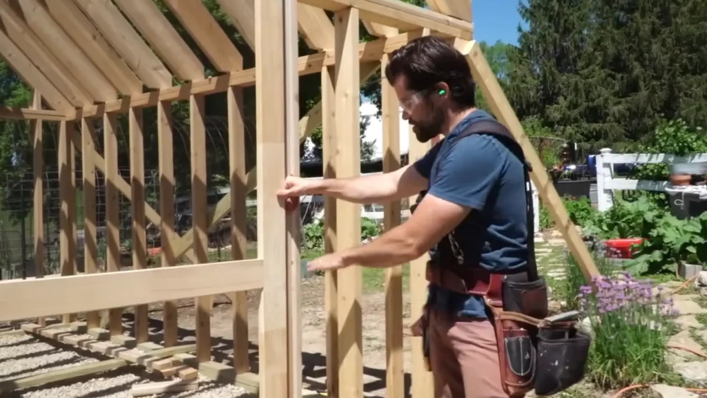 Person pointing at a vertical beam beside a partially framed structure on a construction site.