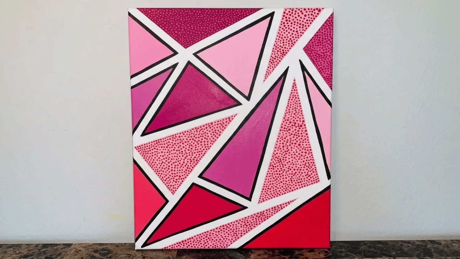 A bold geometric canvas painting with pink triangles, dotted textures, and sharp black outlines on a white background.