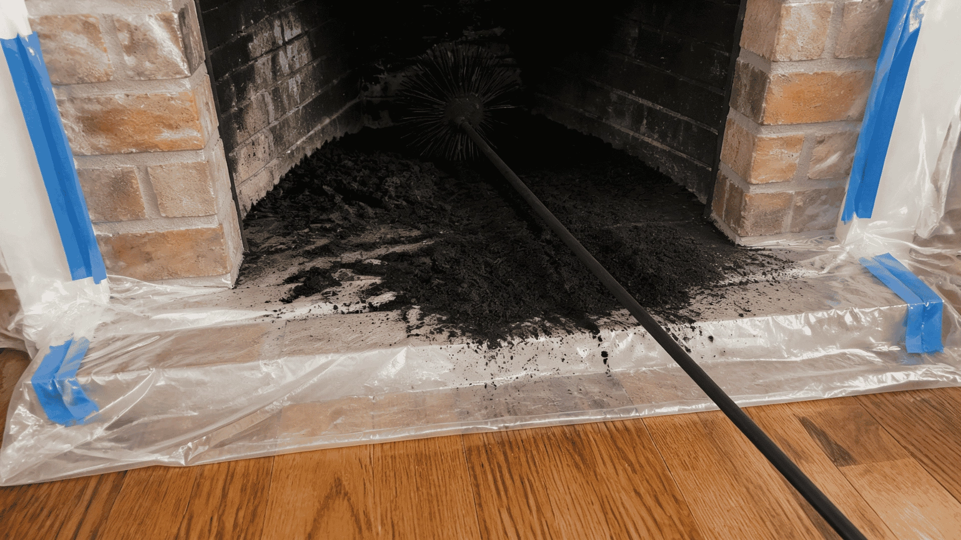 a-chimney-brush-cleaning-a-pile-of-soot-inside-a-brick-fireplace-with-plastic-sheeting-protecting-the-floor