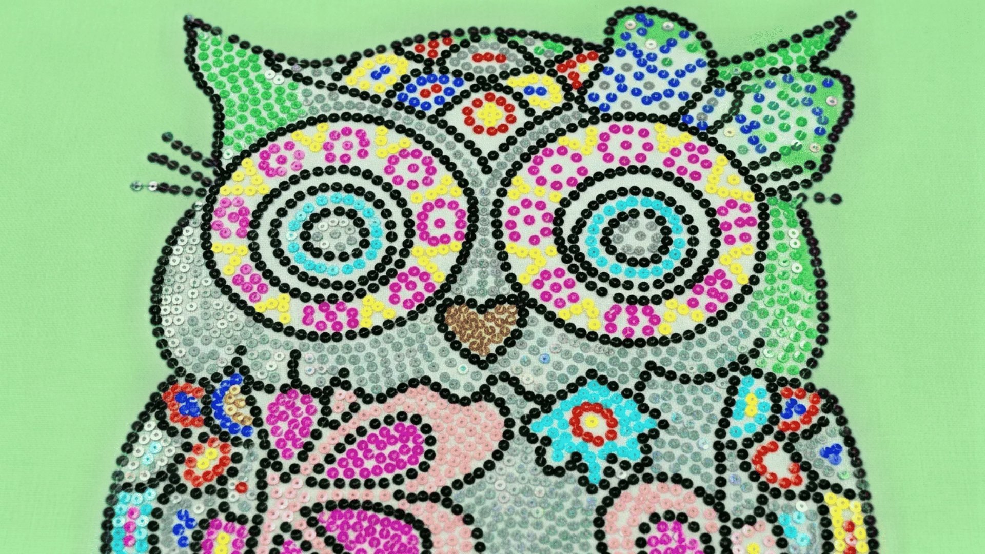 A colorful owl design made with shiny sequins and detailed floral patterns on a bright green background.