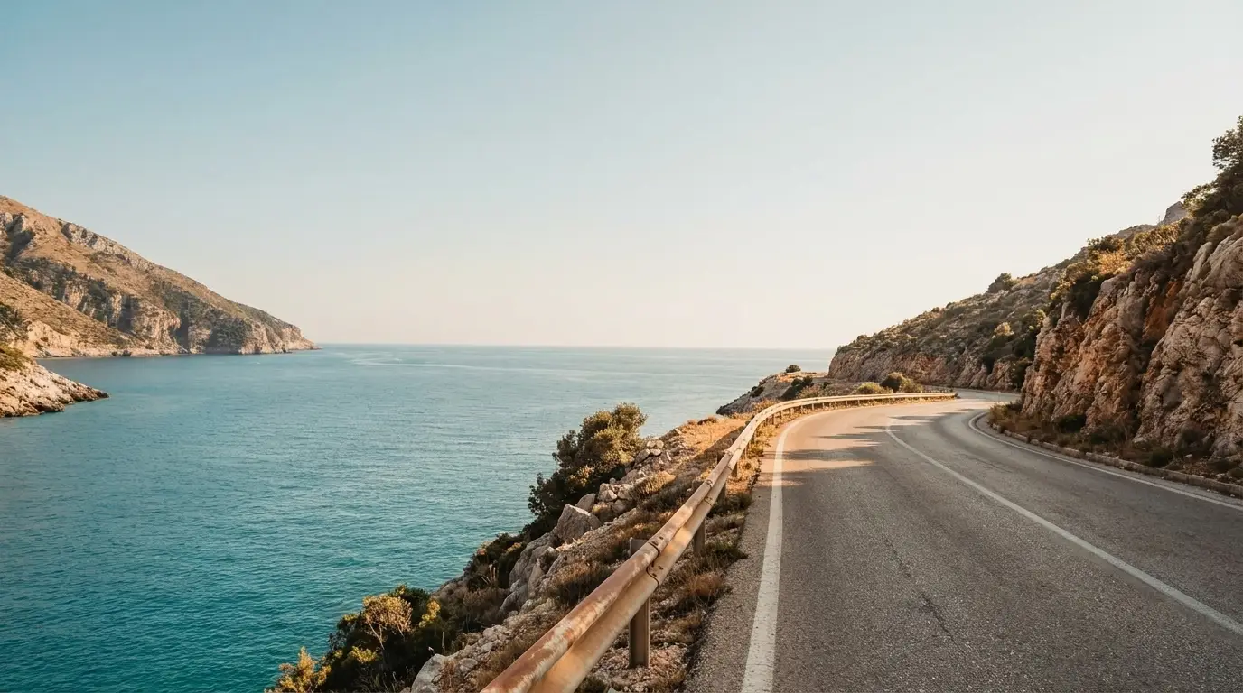 Coastal road curving along rocky cliffs under clear blue sky next to calm sea