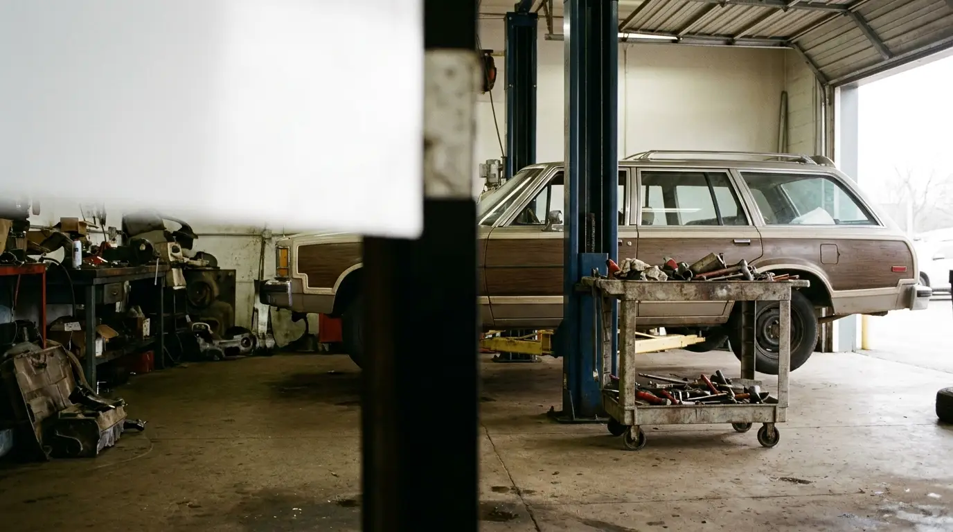 Station wagon on lift in cluttered auto repair garage with tools on cart