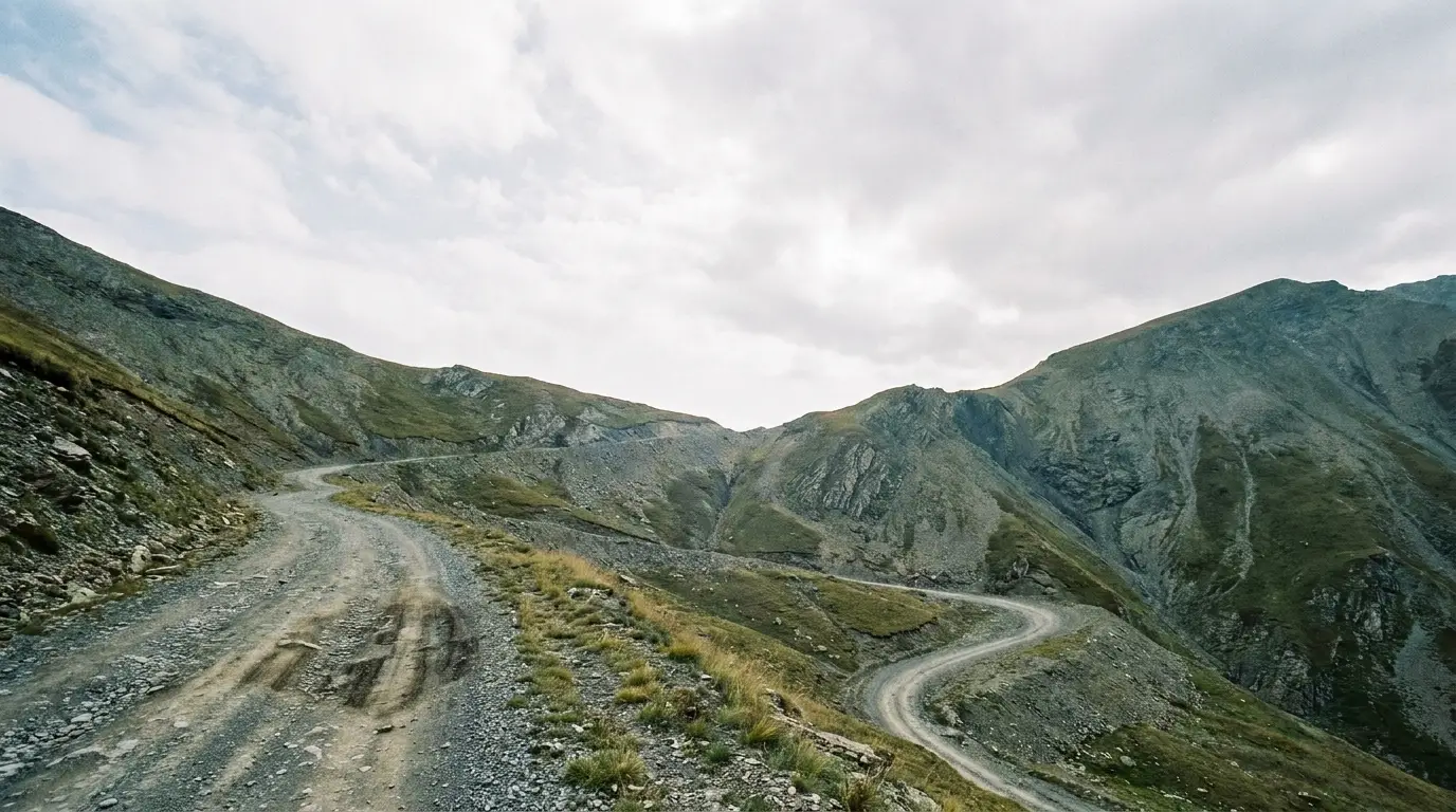 Winding dirt road through rocky mountain landscape under cloudy sky