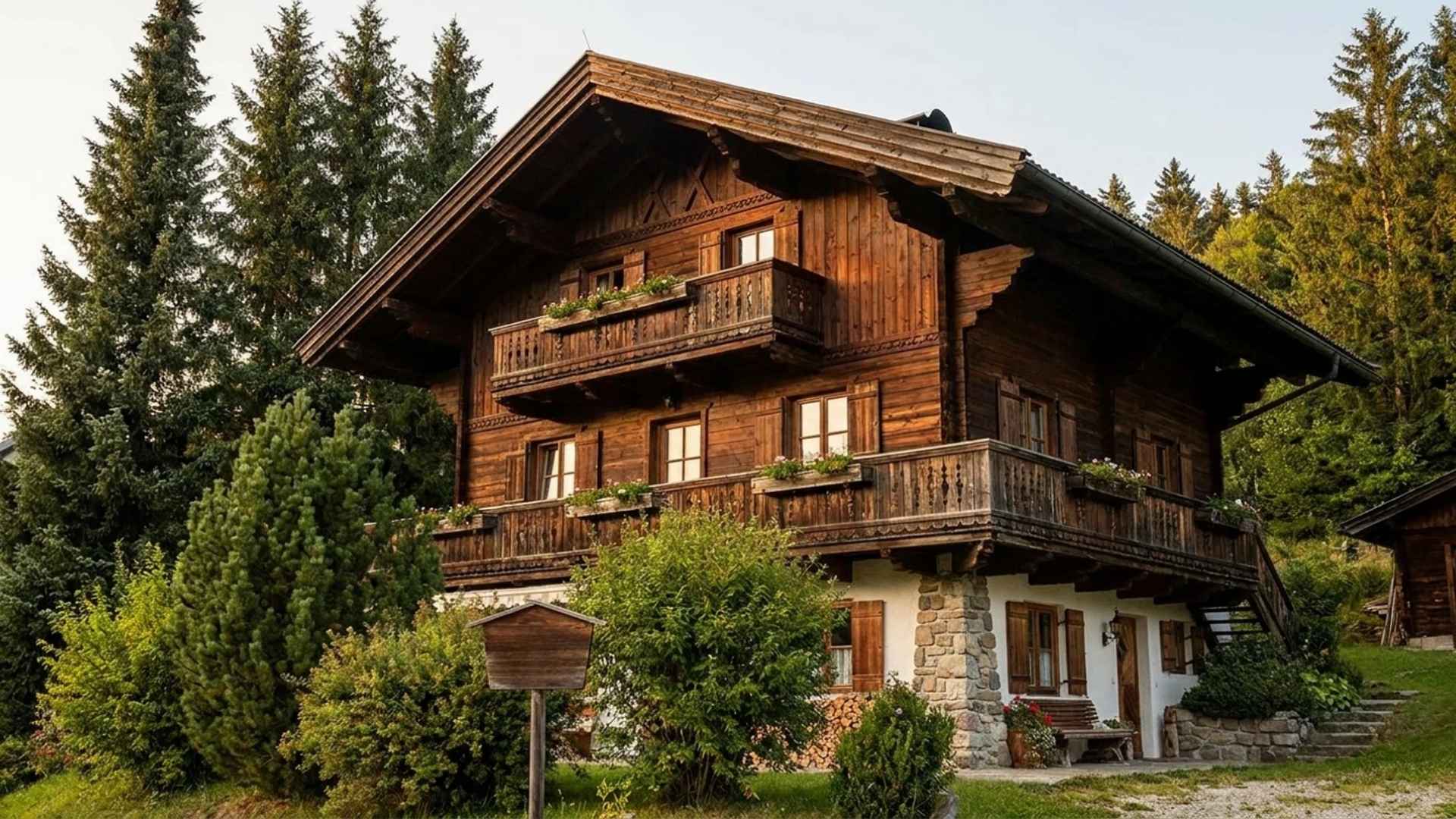 Traditional Alpine chalet with timber balconies, surrounded by pine trees and mountains.