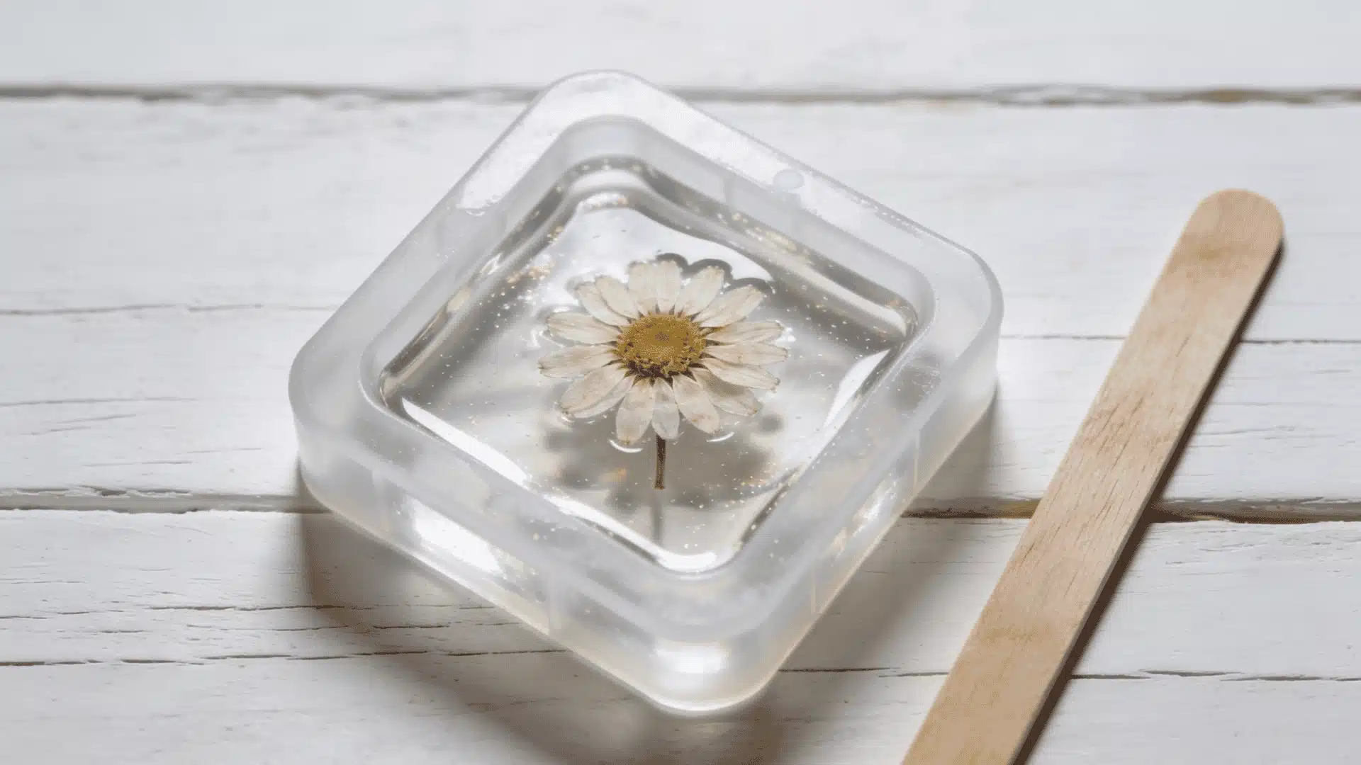Clear silicone mold filled with transparent resin and a small dried daisy on a white wooden surface