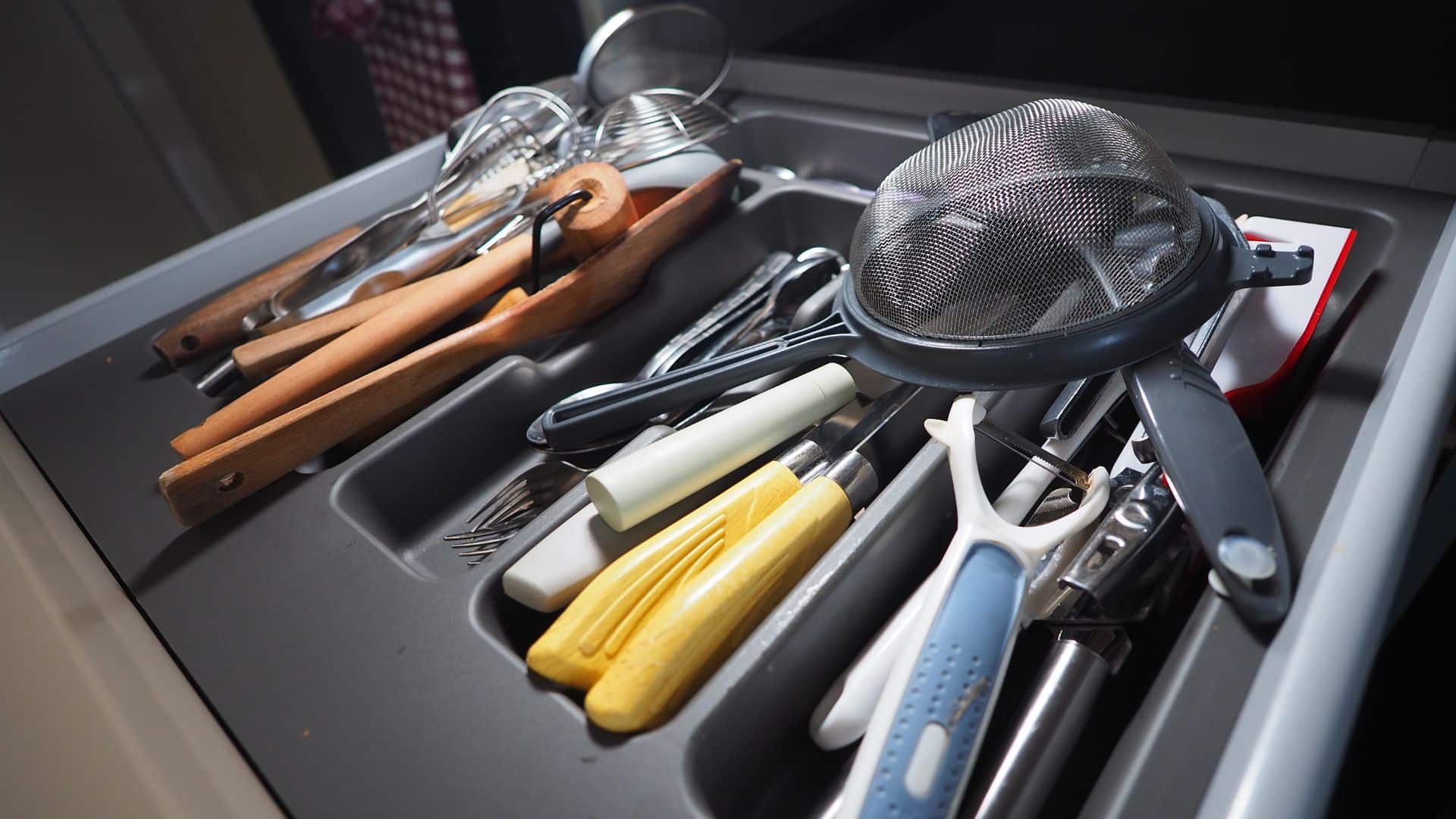 Cluttered utensil drawer with mixed tools and dividers, showing a real example for how to organize kitchen drawers efficiently and neatly