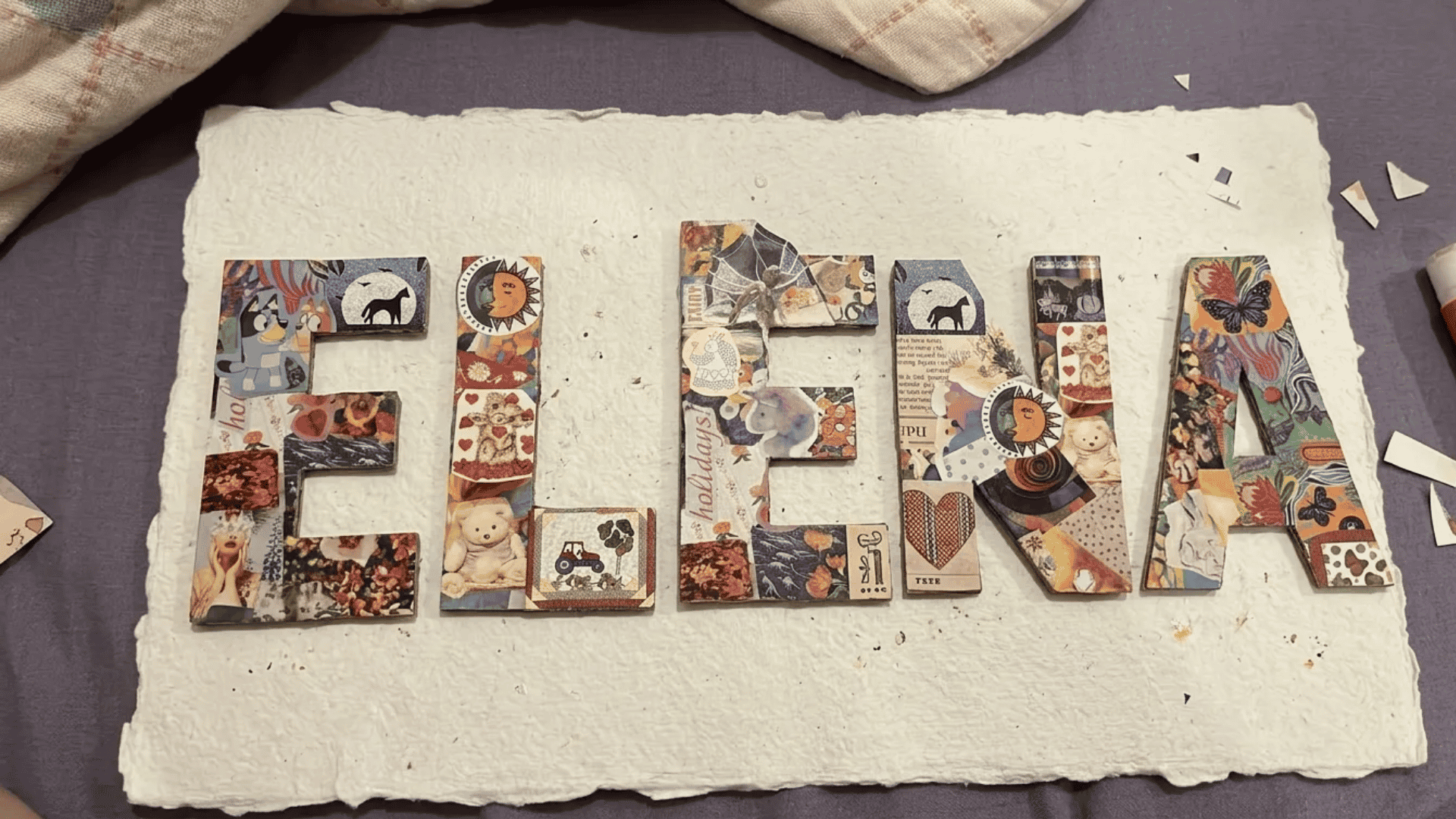 Collage name art with colorful magazine cutouts and decorative patterns on textured handmade paper.