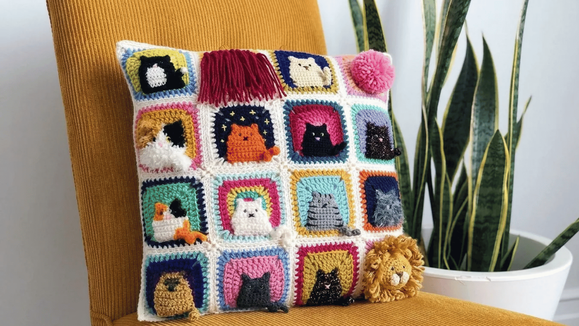 Colorful crochet pillow cover featuring playful cat-themed granny squares placed on a mustard-yellow chair beside indoor plants.