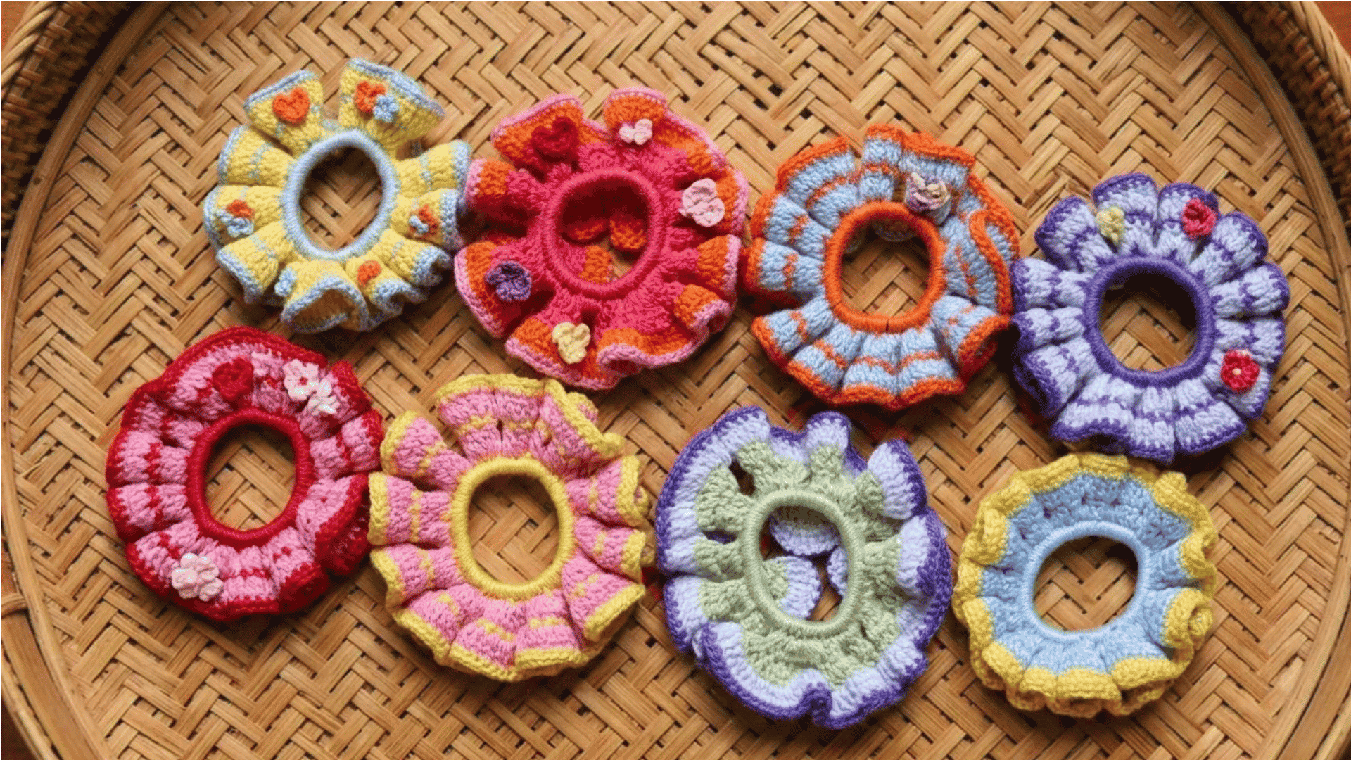 Colorful handmade crochet scrunchies with playful ruffled patterns arranged on a woven bamboo tray.