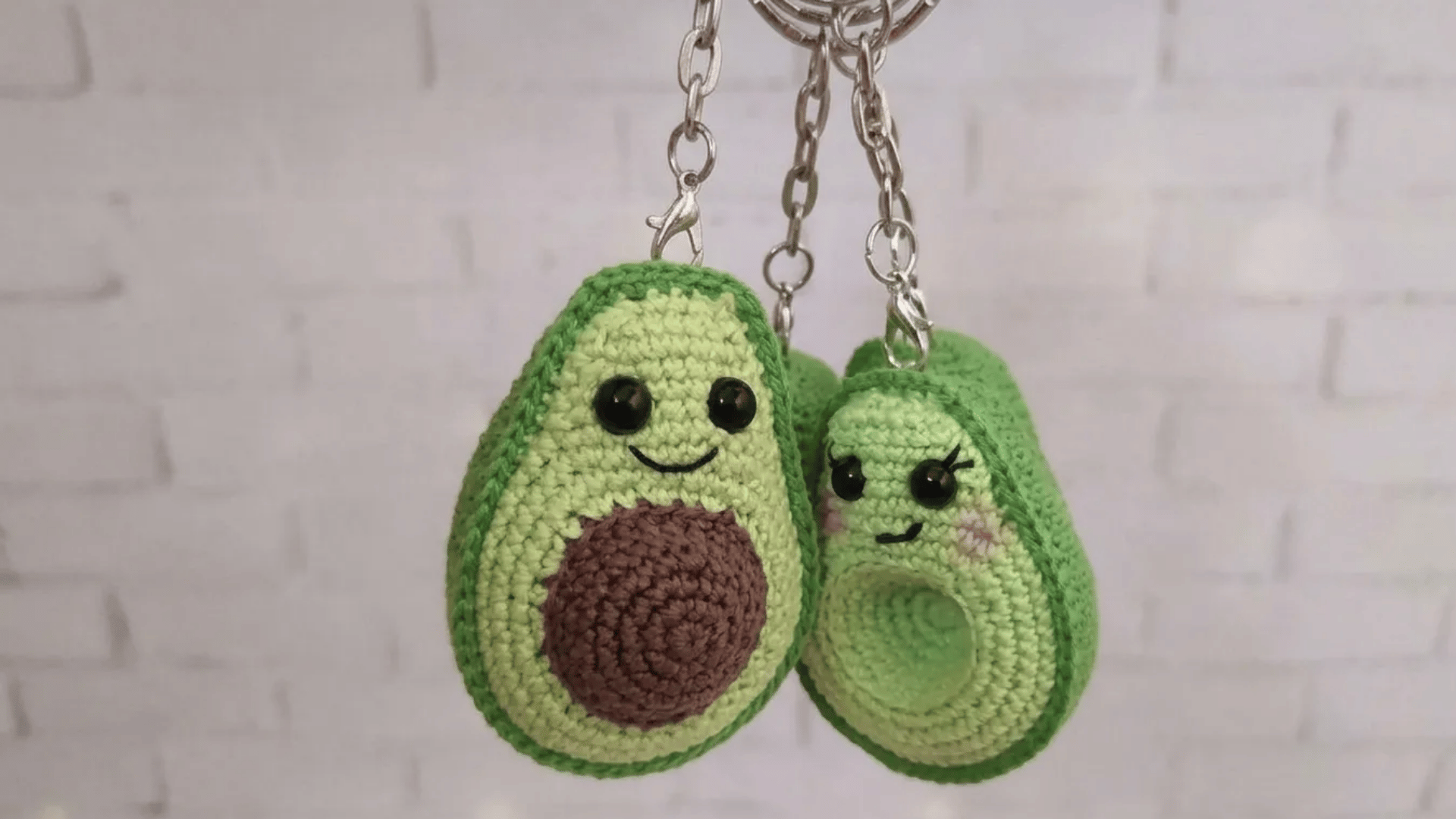Cute crochet avocado keychains with smiling faces hanging from silver chains against a soft neutral background.