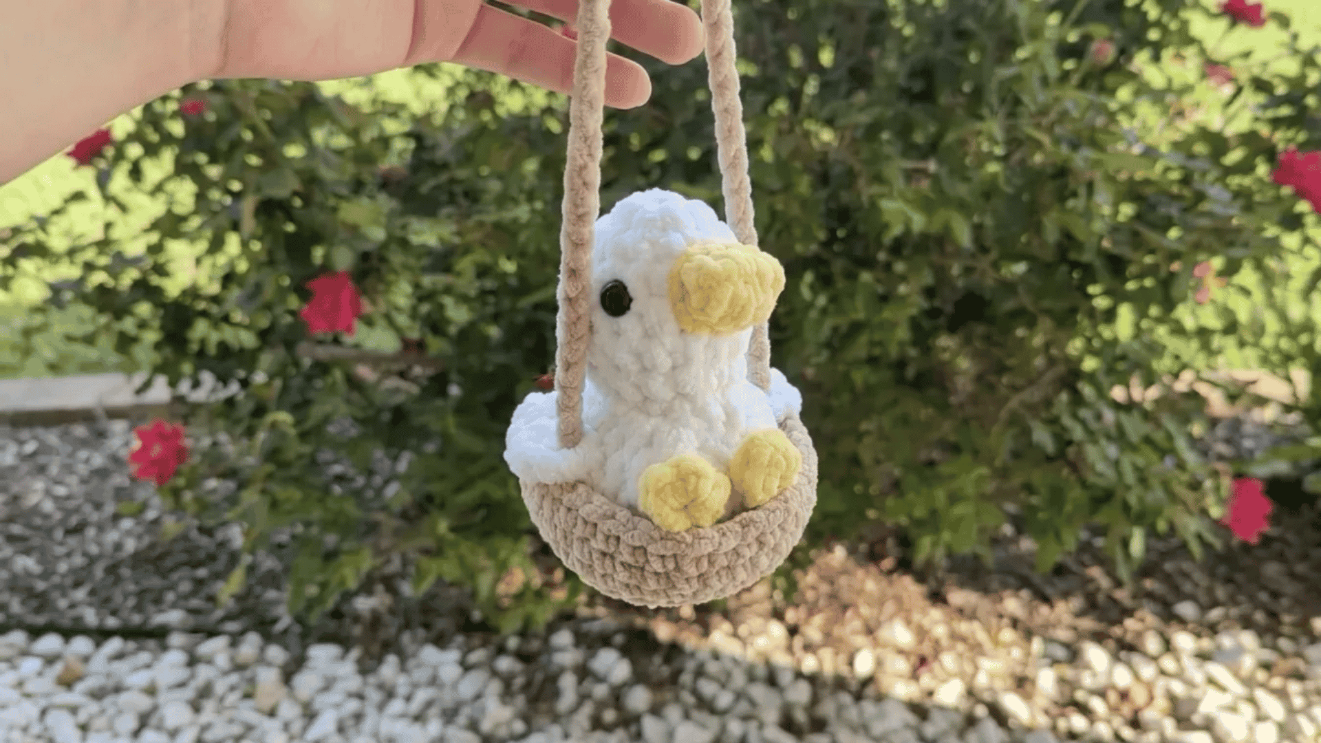 Cute handmade crochet duck plushie sitting in a small hanging basket against a garden background.