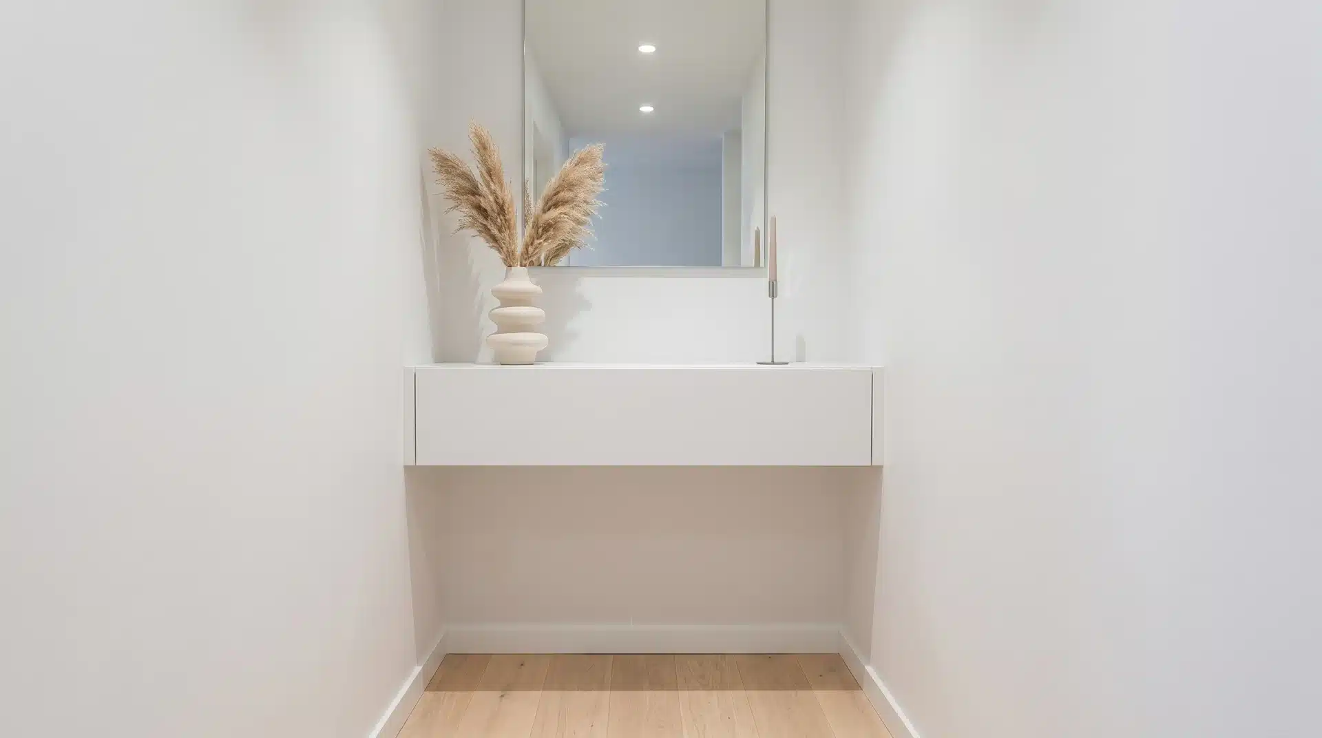 White floating console table mounted to a wall, styled with a ribbed ceramic vase of dried pampas grass and a mirror above.
